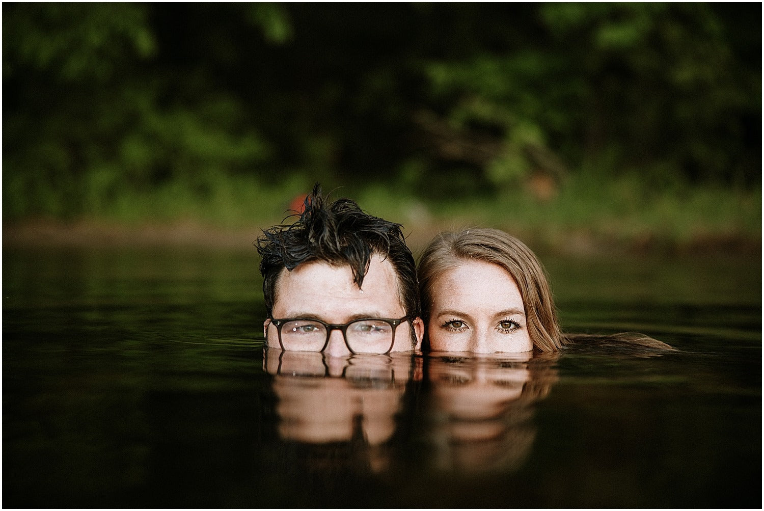 Couples posing from a lakeside with only half heads above the water