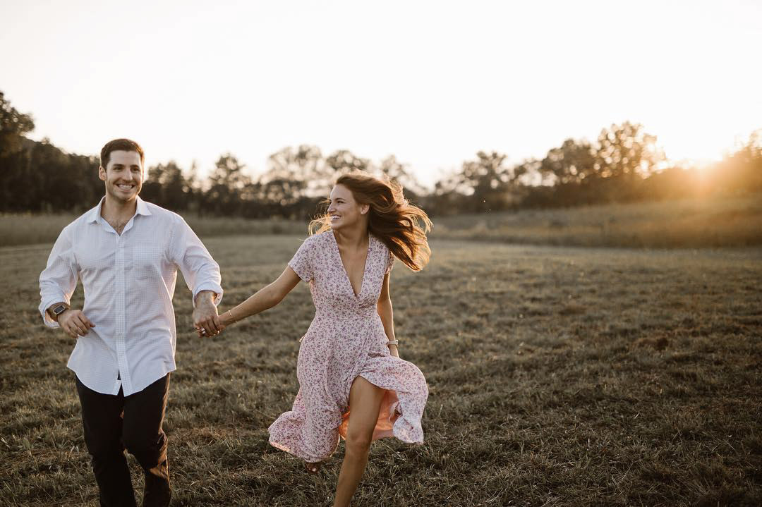 a couple running through a grassy field while the sun rises behind them