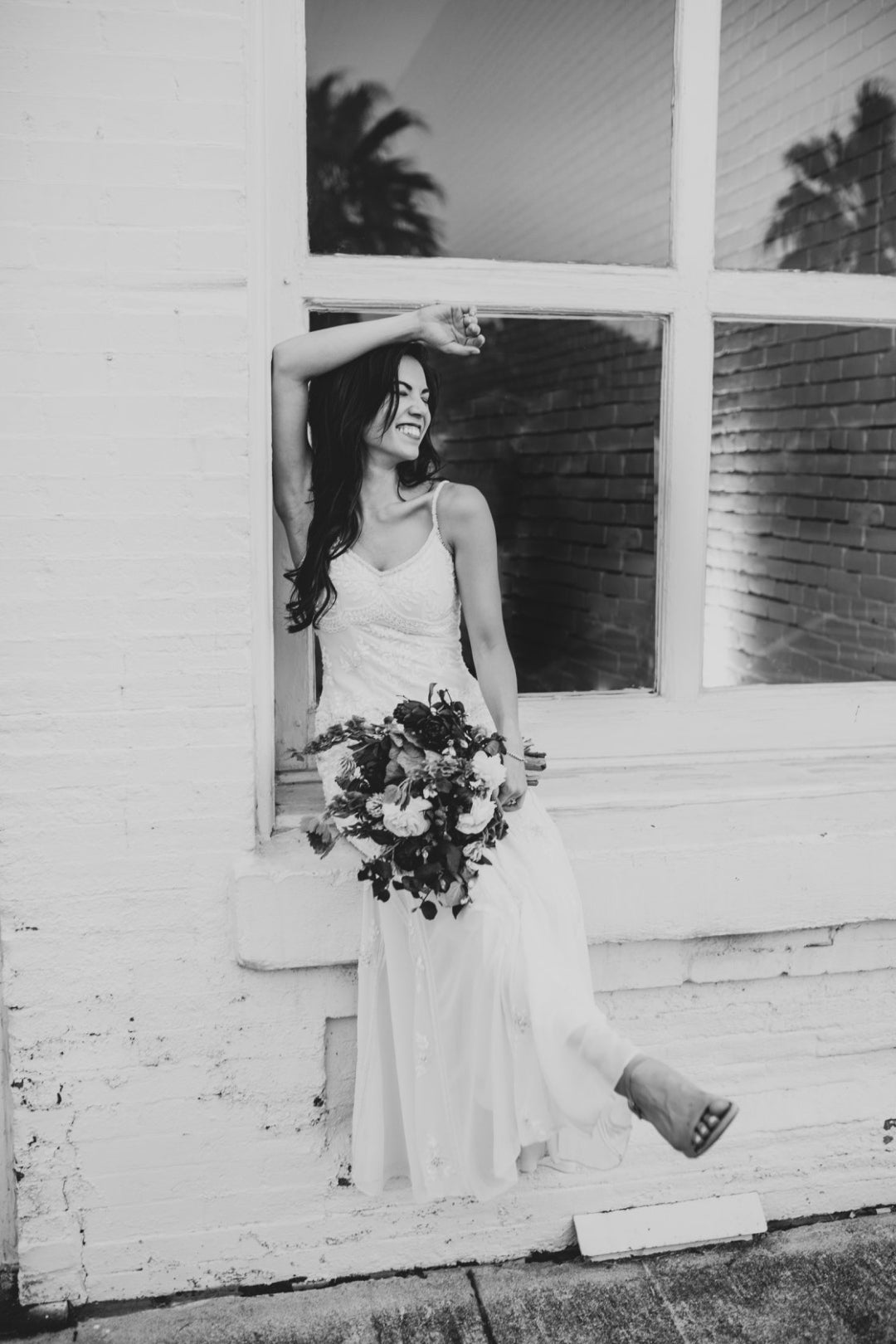 Black and white photo of a bride holding a bouquet while posing in front of a window