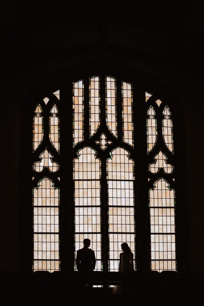 a silhouette image of the bride and groom standing in front of a big church window