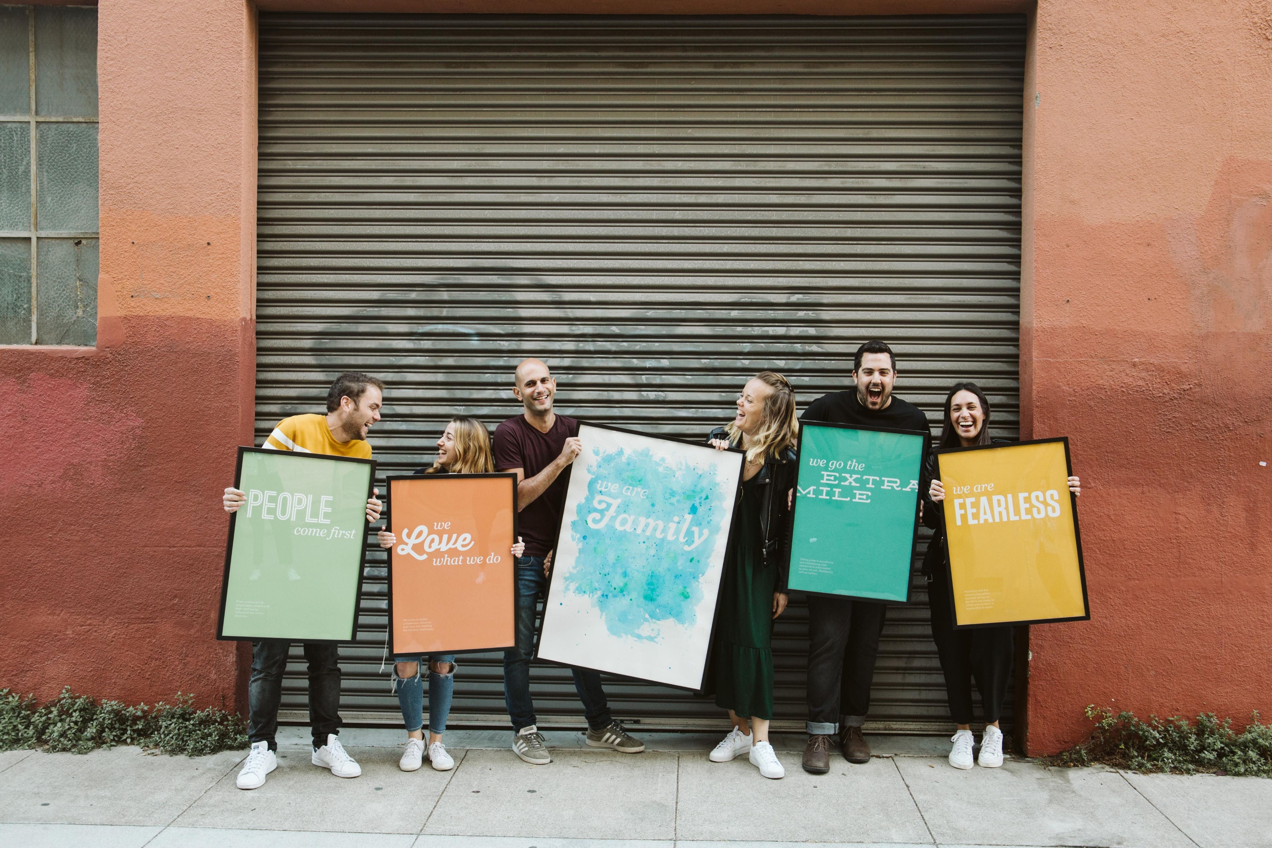 Six people displaying different core values of HoneyBook by holding different poster boards