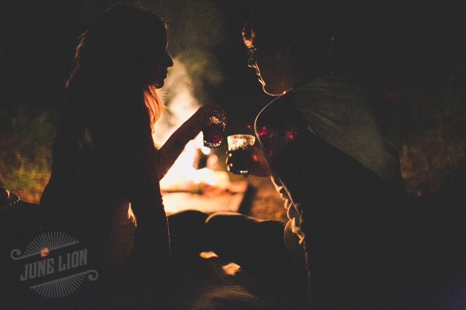 A couple sitting in front of a bonfire doing cheers