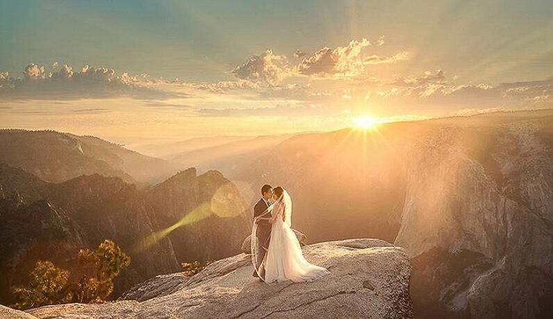 a couple embracing each other standing on the edge of a cliff during sunset