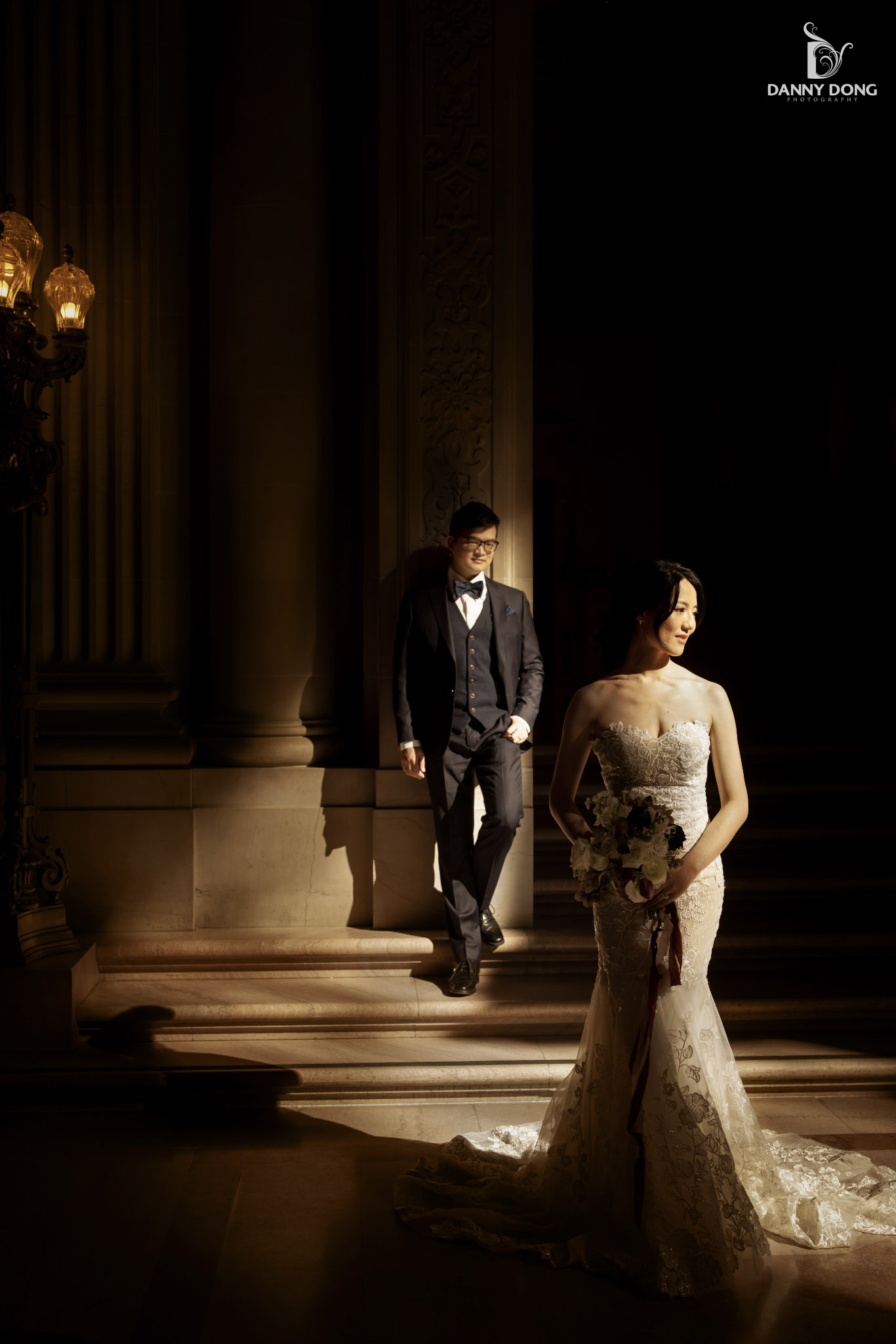 a bride standing in wedding attire while the groom looks at her from behind