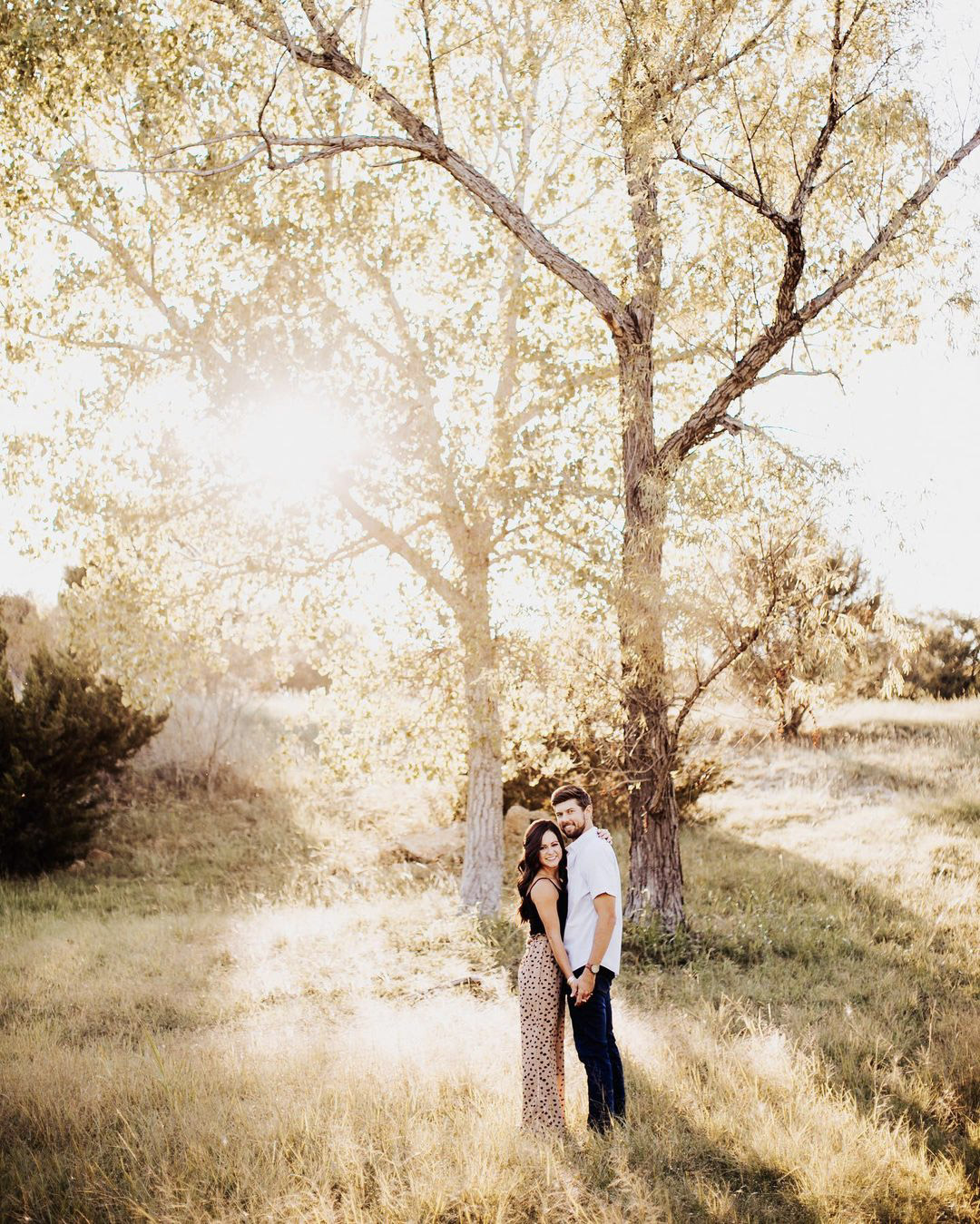 a couple standing closely on a grassland with the sun shining behind them