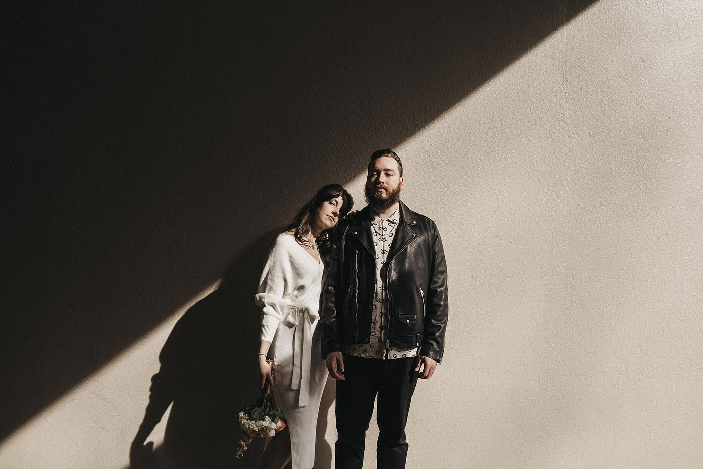 a couple standing in front of a wall with shadow falling on it diagonally