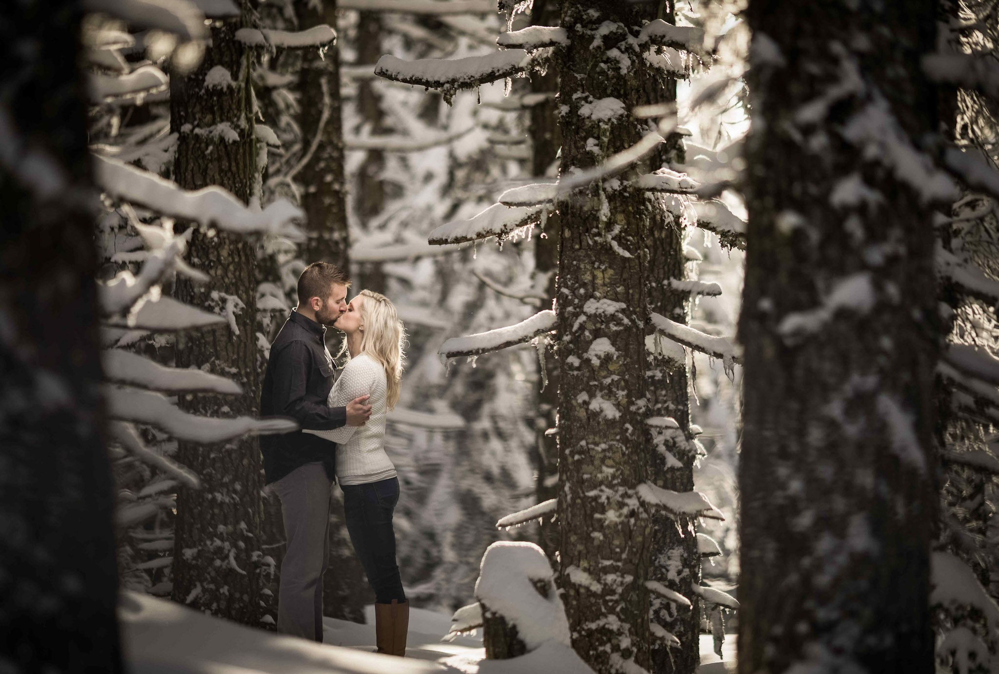 a couple kissing in the middle of a forest with the ground and tree leaves covered in snow