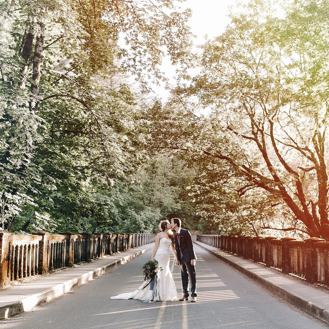 a couple kissing in the middle of a road with trees on either side