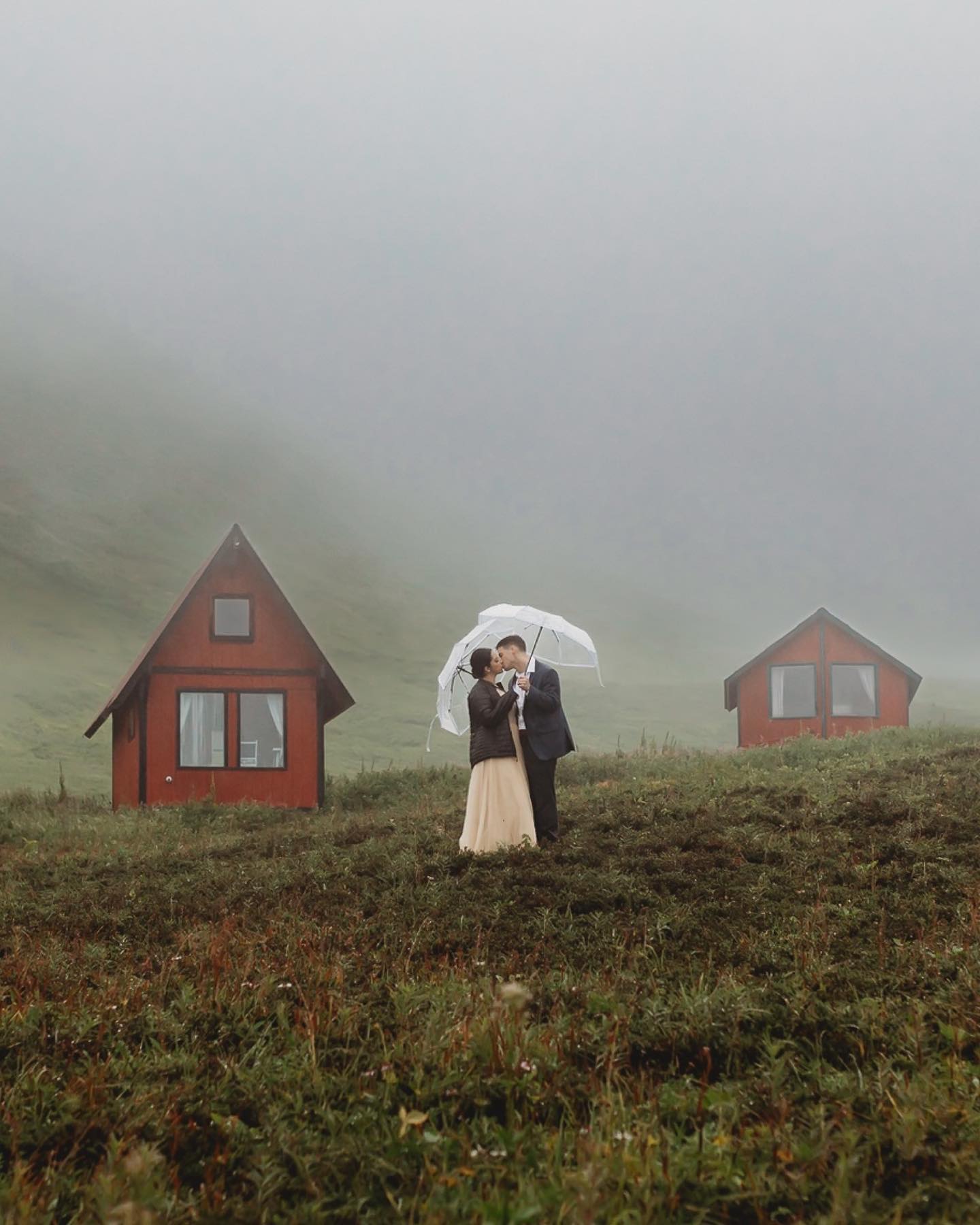 a wedding couple standing holding an umbrella during rain in a foggy quaint little village