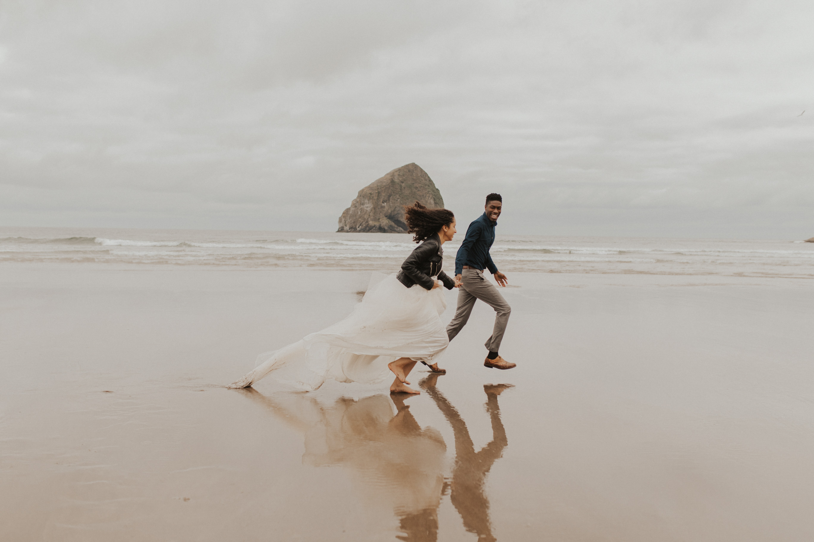 A bride and groom running on the beach as the waves crash at the background