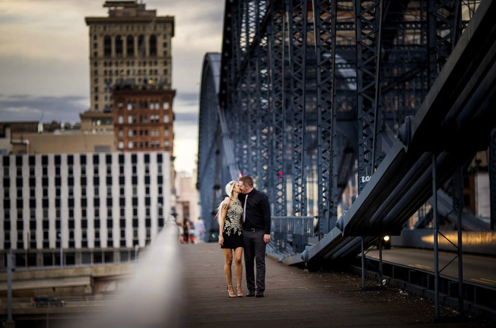 a couple walking and kissing by the side of a bridge