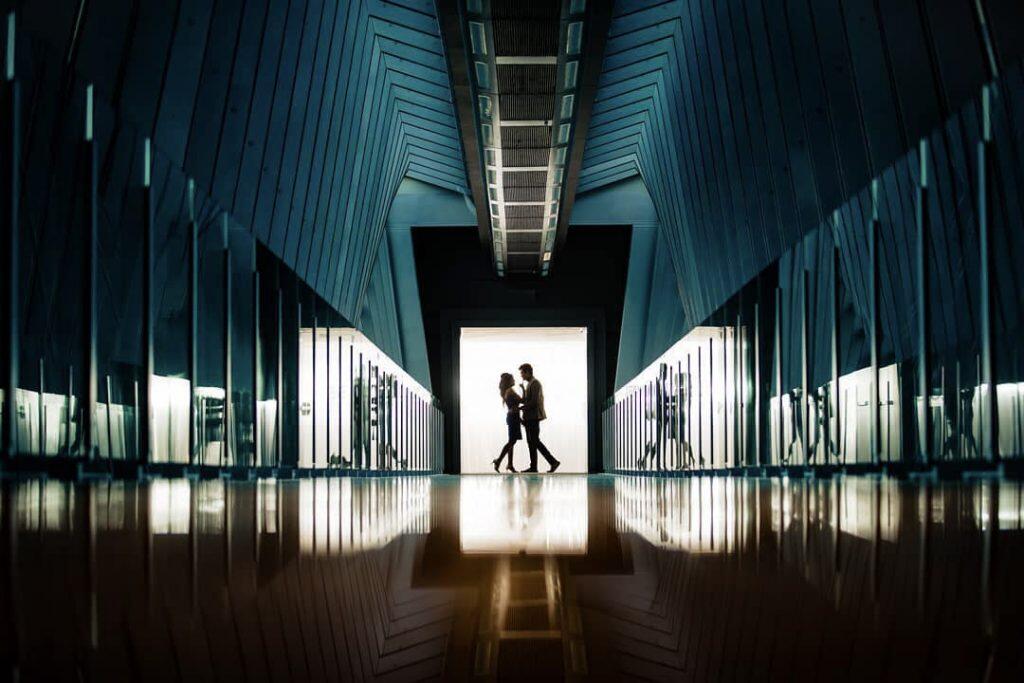 a couple posing holding each other at the end of a reflective corridor