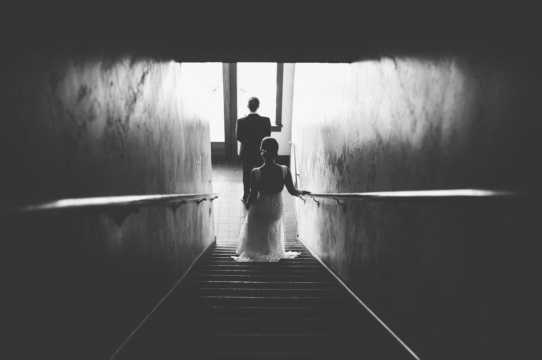 A first look moment where the groom awaits looking towards the window as the bride walks down the stairs from behind