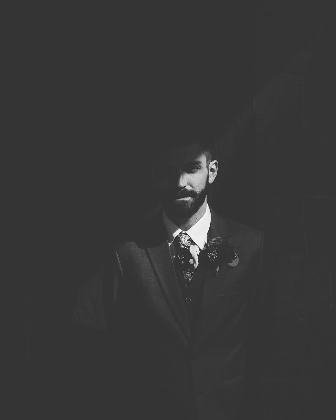 A monochrome portrait of a groom standing beside a wall as half of his face is in shade 