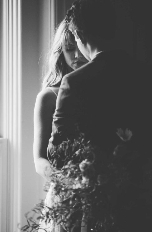 An over the shoulder shot of bride and groom hugging in front of a window