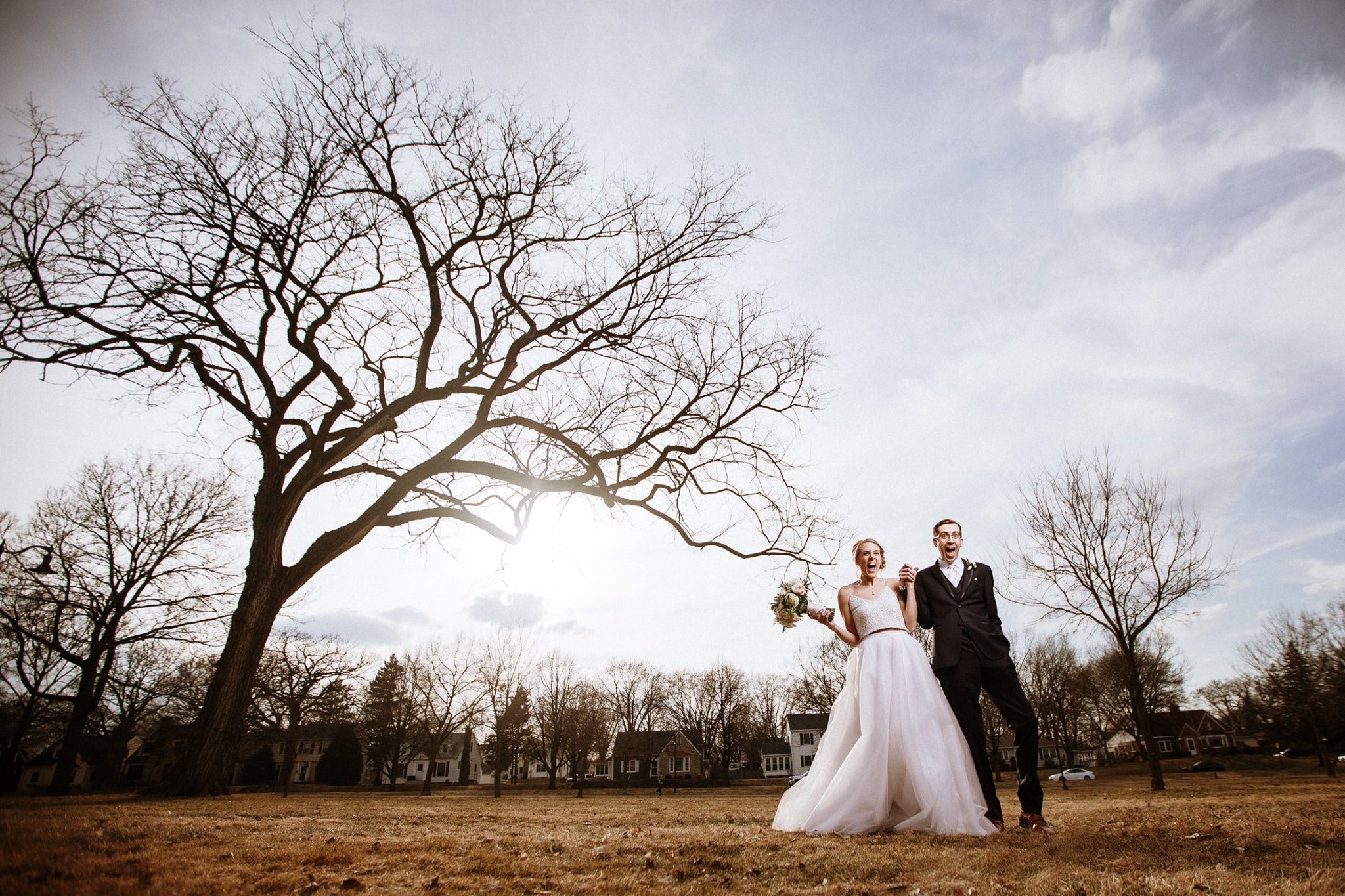 A bride and groom holding hands and standing by the side of a dried up tree