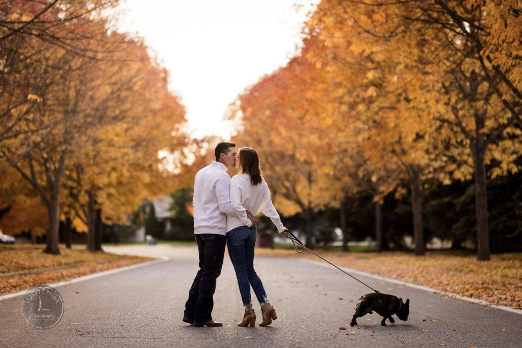 a couple standing in the middle of the road kissing holding their pet dog