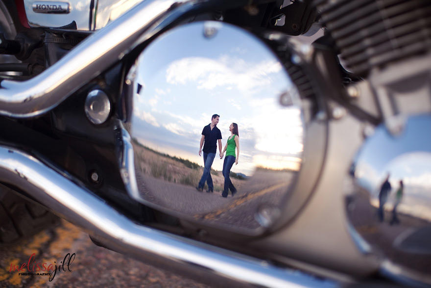 A reflection on a motorcycle of a couple holding hands and walking during their engagement session photos.