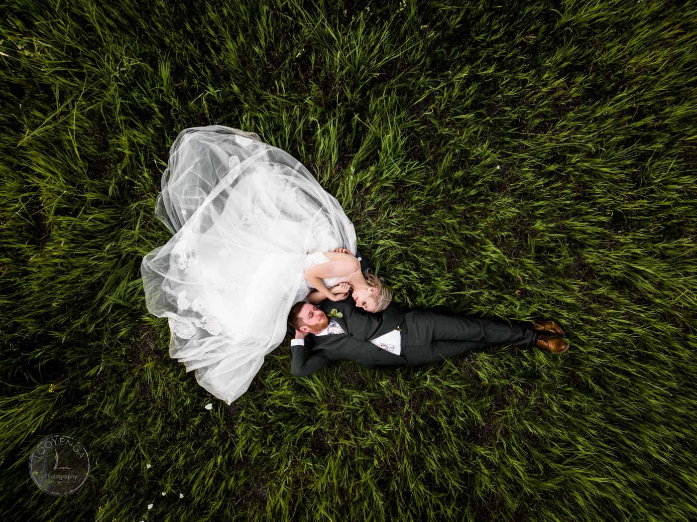 a top down shot of a wedding couple lying down on the grass in their wedding attire