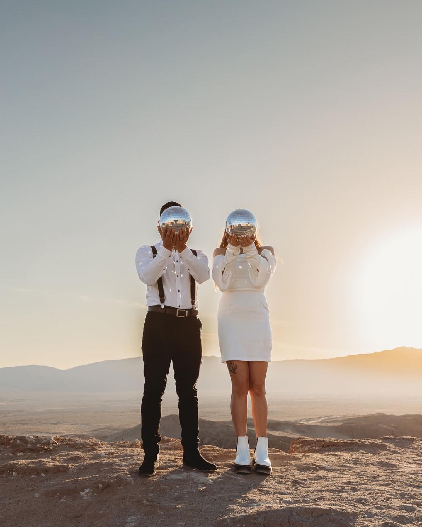 a wedding couple in quirky outfit standing with shiny spheres in front of their faces