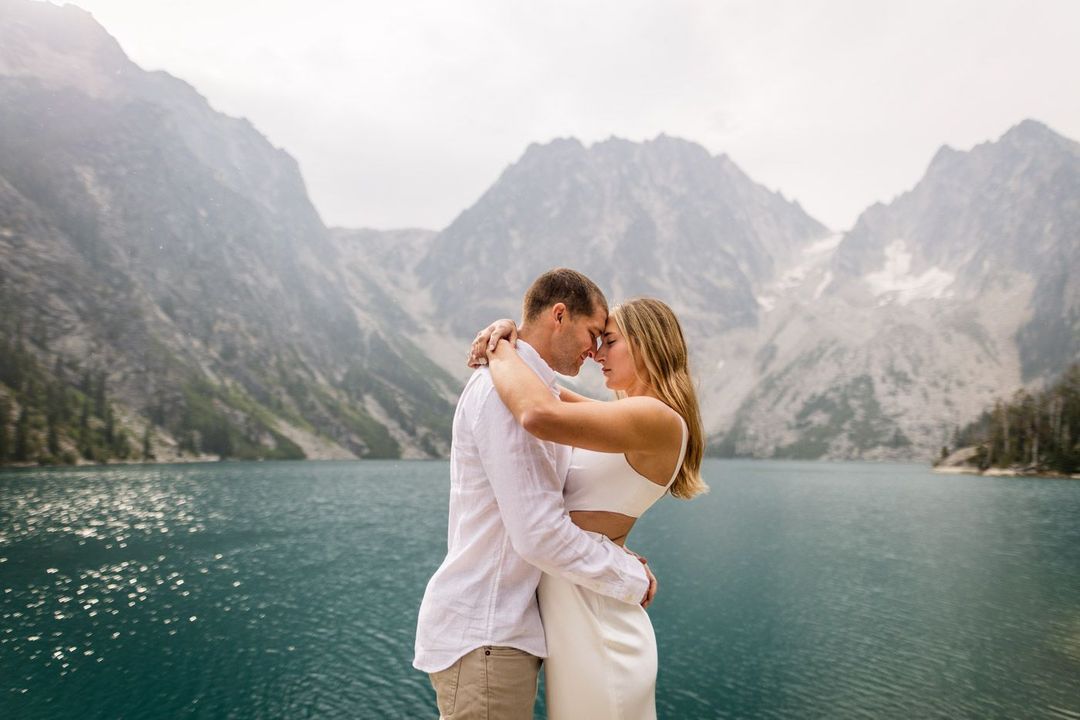 a couple embracing each other in front of a lake surrounded by mountains