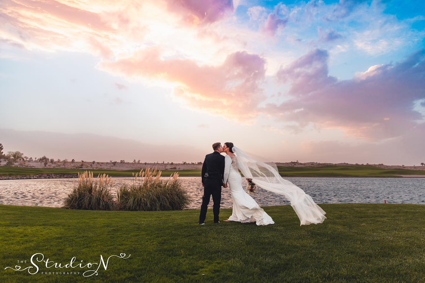 a wedding couple kissing in front of a lake with beautiful skies behind them