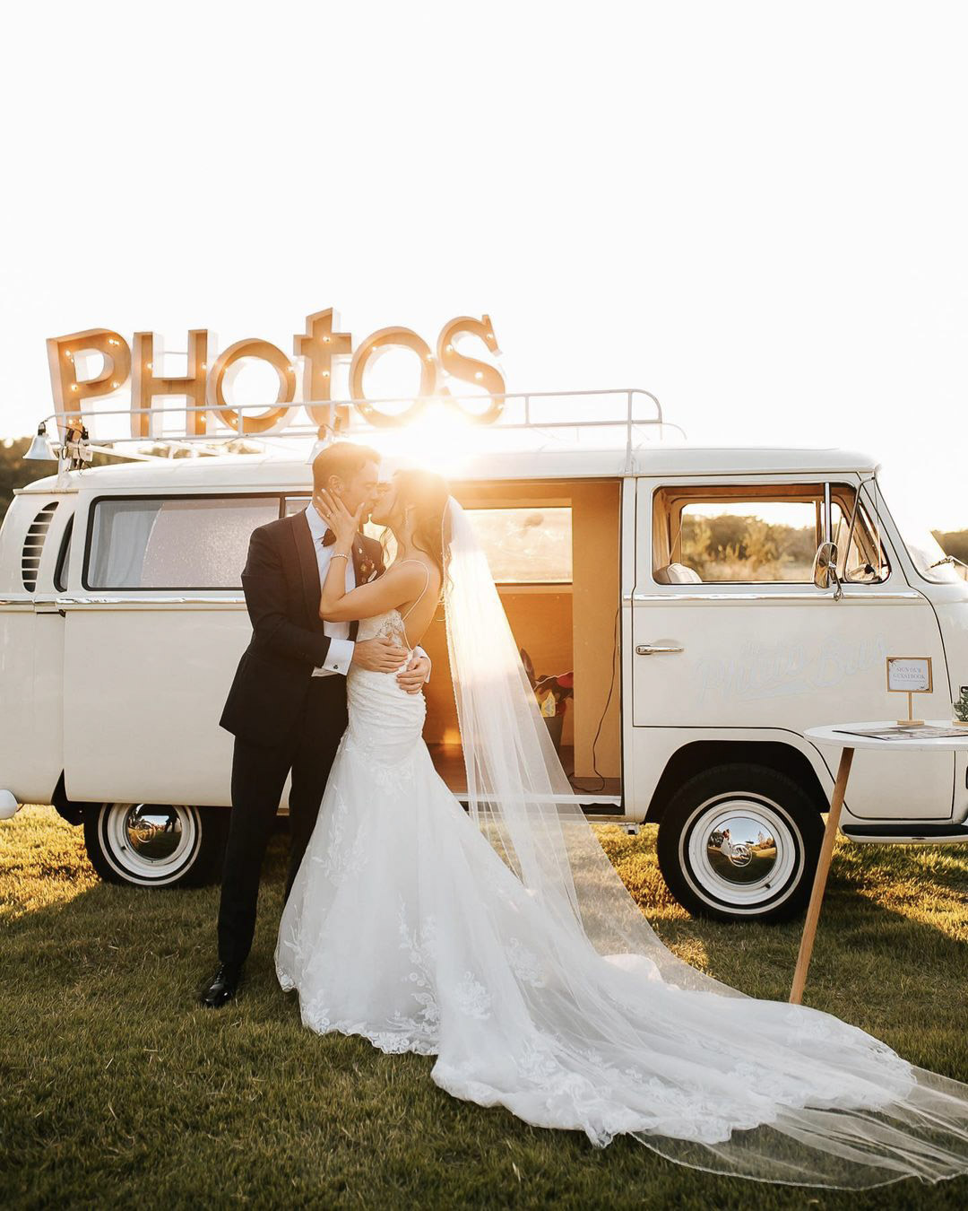 a wedding couple kissing while the sun shine behinds them in front of a mini van 