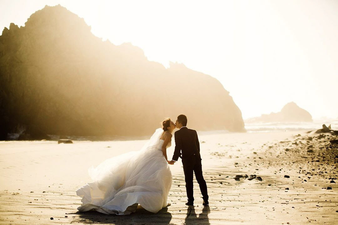 a wedding couple kissing on the beach under the bright golden hour sun