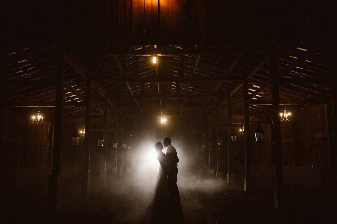 a couple standing in a dimly lit area with a light shining brightly behind them