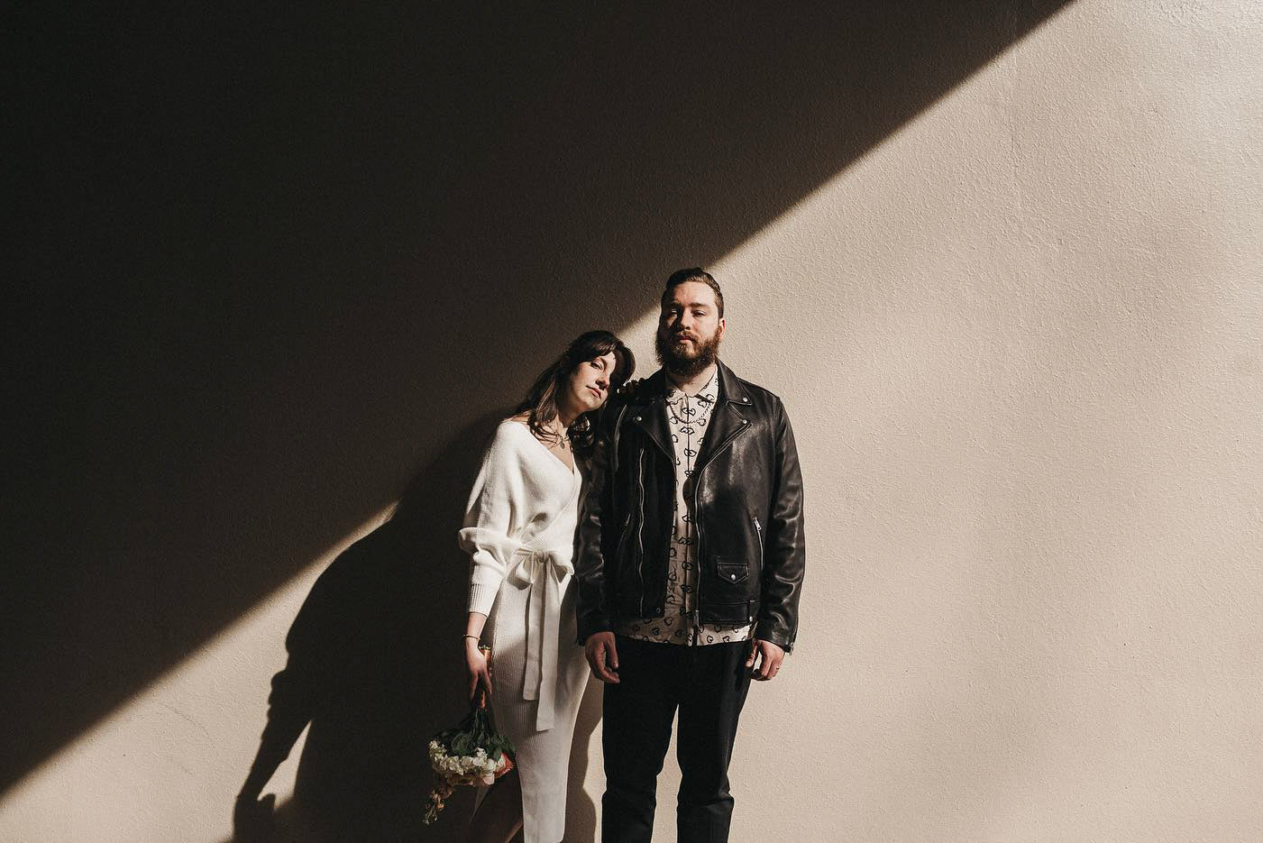 a couple posing in front of a wall with diagonal shadows