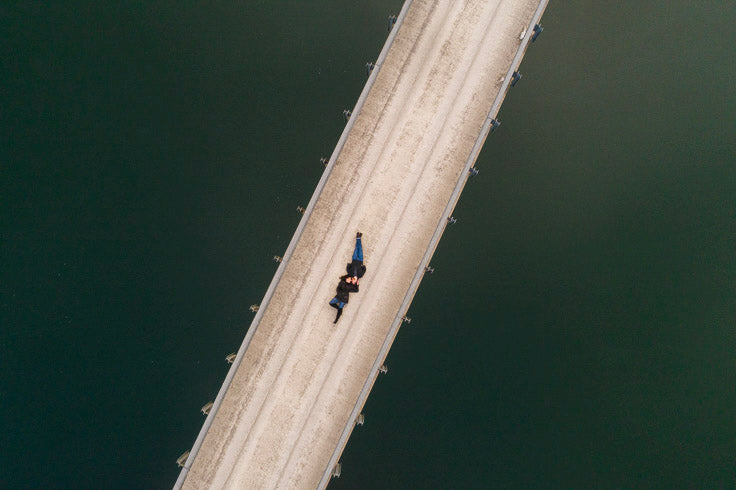 an aerial top down shot of couple lying down on a bridge surrounded by water