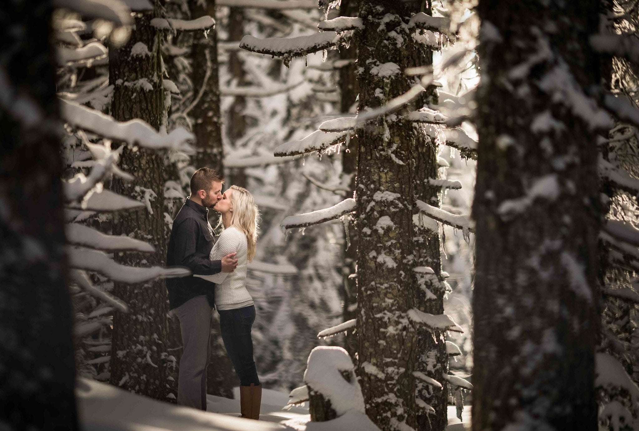 a couple kissing in the middle of the woods covered in snow