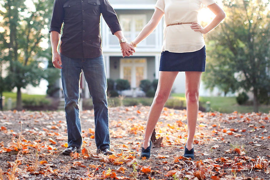 A couple holding hands, with the camera cut off at their chests, with leaves fallen on the ground and natural light in the background.