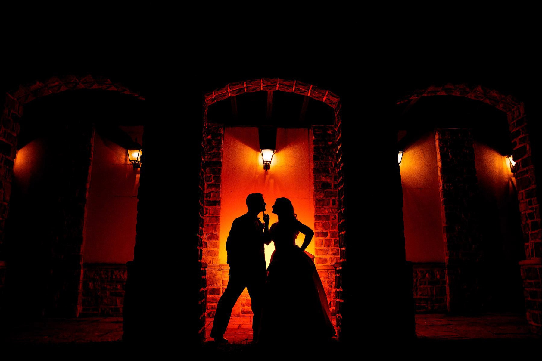 a silhouette of couple posing in front of a brick wall