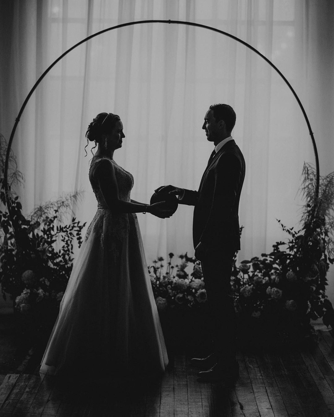 a black and white portrait of a couple holding hands in front of the wedding aisle arch