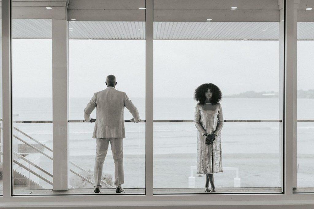 a bride and groom standing in front of a clear glass balcony facing opposite sides