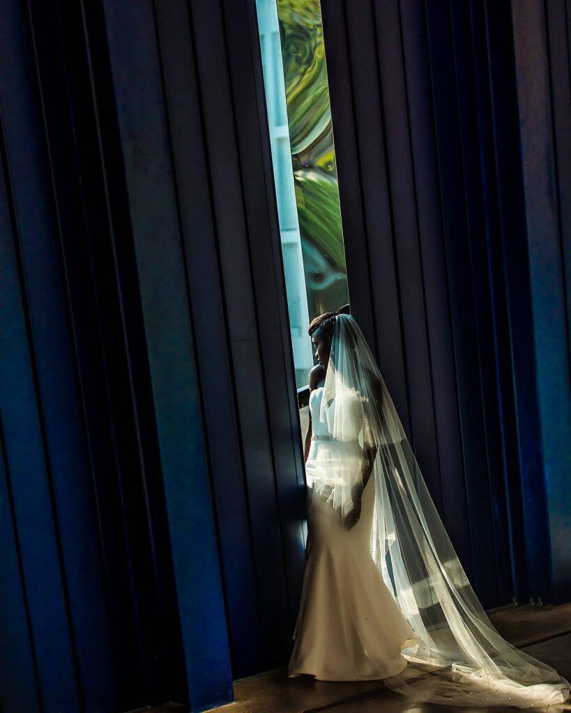 a bride in her wedding dress looking outside through the gap in between huge curtains