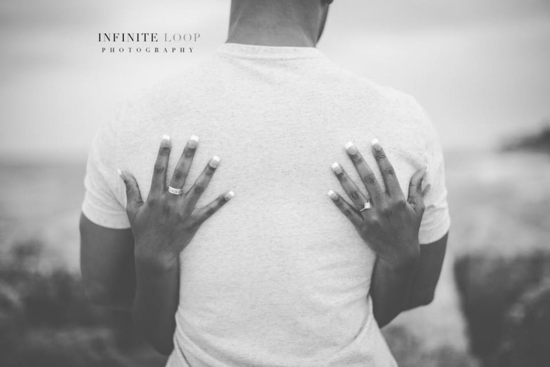 A black and white photo of a bride's hand resting on the groom's back as they hug 