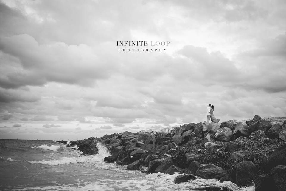 a couple kissing each other standing on rocky boulders with waves crashing around them 