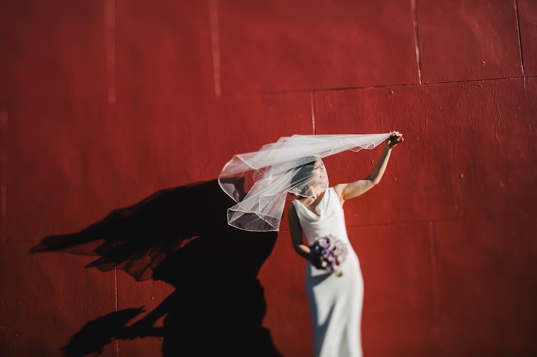 A bride posing in front of a red wall with her