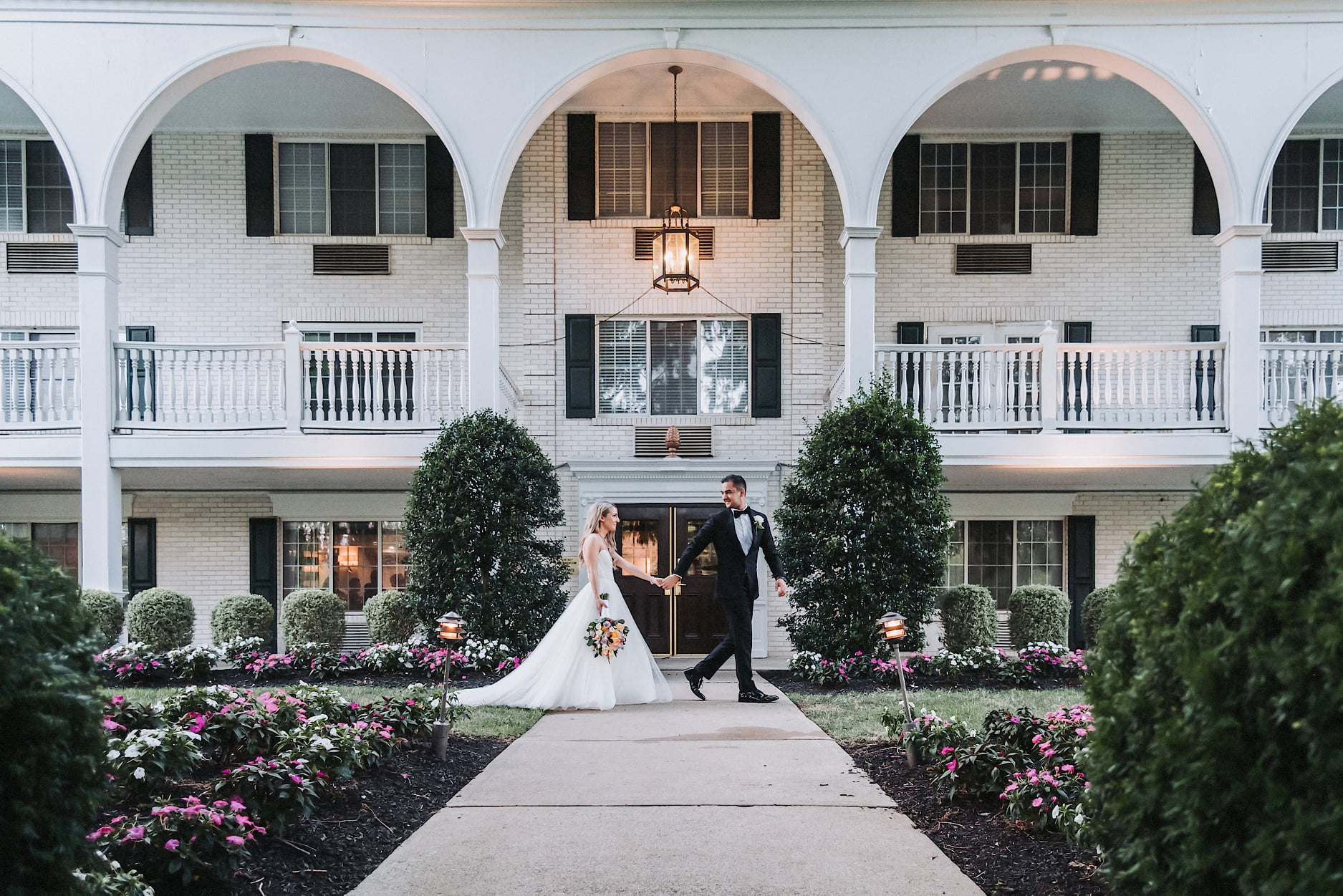 a wedding groom leading the bride through the front lawn by the hand in their wedding attire