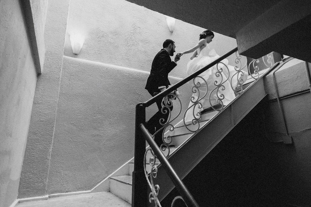 a bride leading the groom through a staircase holding his hand