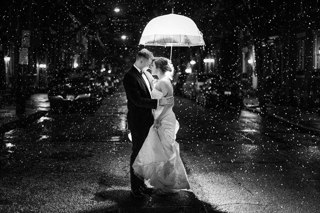 Bride and groom posing under an umbrella as the rain creates a beautiful background