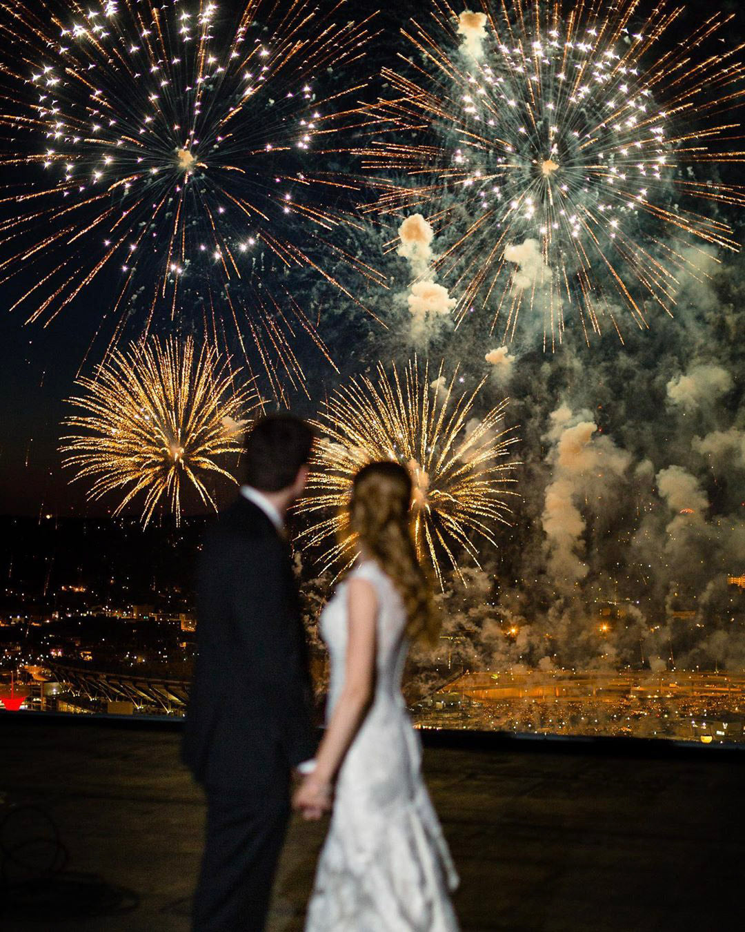 a married couple holding hands and looking at a firework show