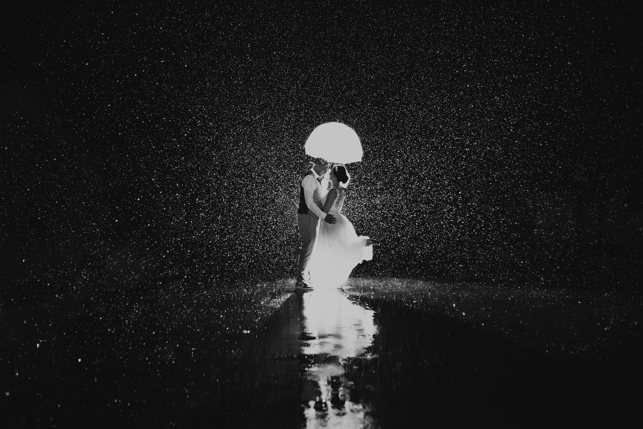 A couple posing under an umbrella as the rain creates a beautiful background and reflection on the ground