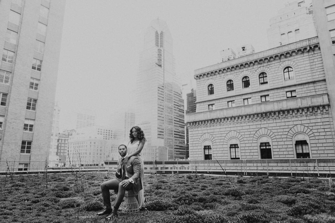 black and white photo of a couple standing on the top of a building with other buildings behind them