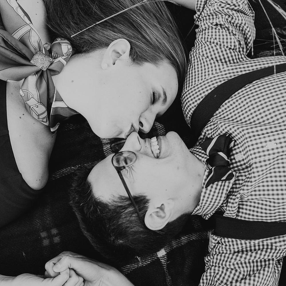 black and white photo of couple laying on ground with woman kissing man's nose