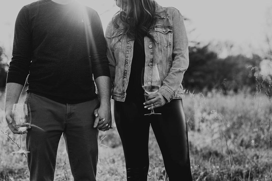 black and white photo of couple holding wine glasses in a field