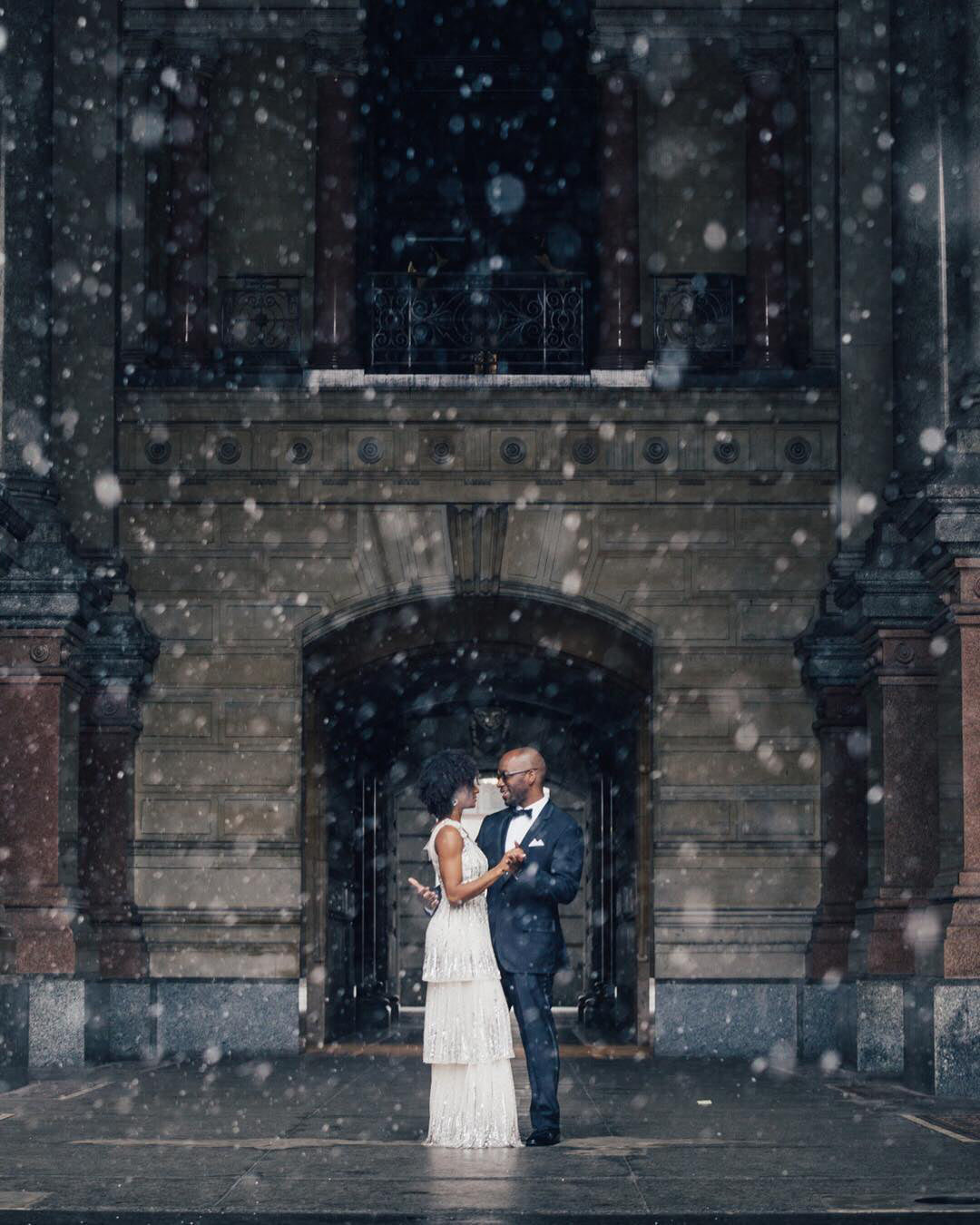 A couple holding each other and looking into each other's eyes while the snow falls around them