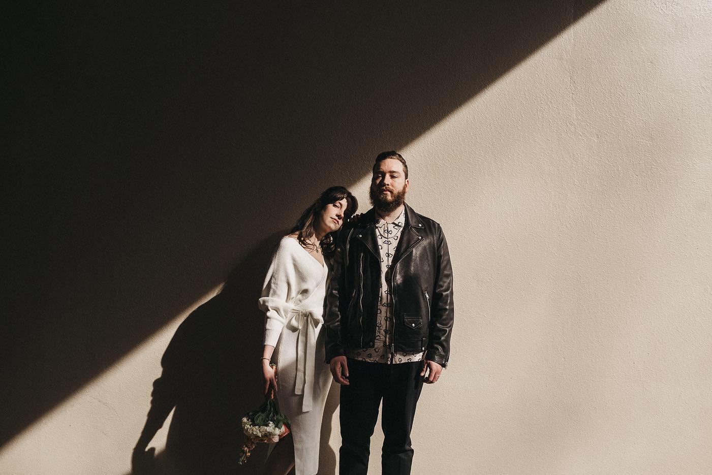 a couple posing standing in front of a wall half covered by a shadow